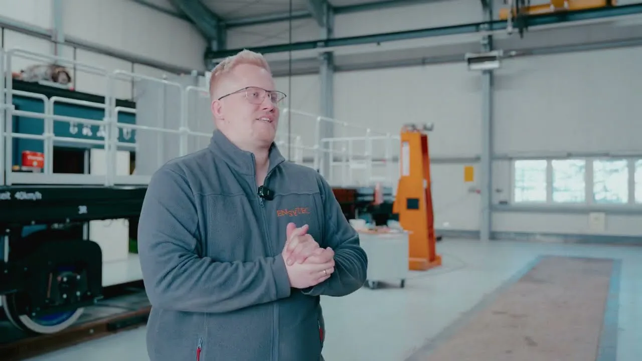 Mitarbeiter im ENSYTEC-Pullover erklärt in der Fertigungshalle die Arbeit an einem Schienenfahrzeug